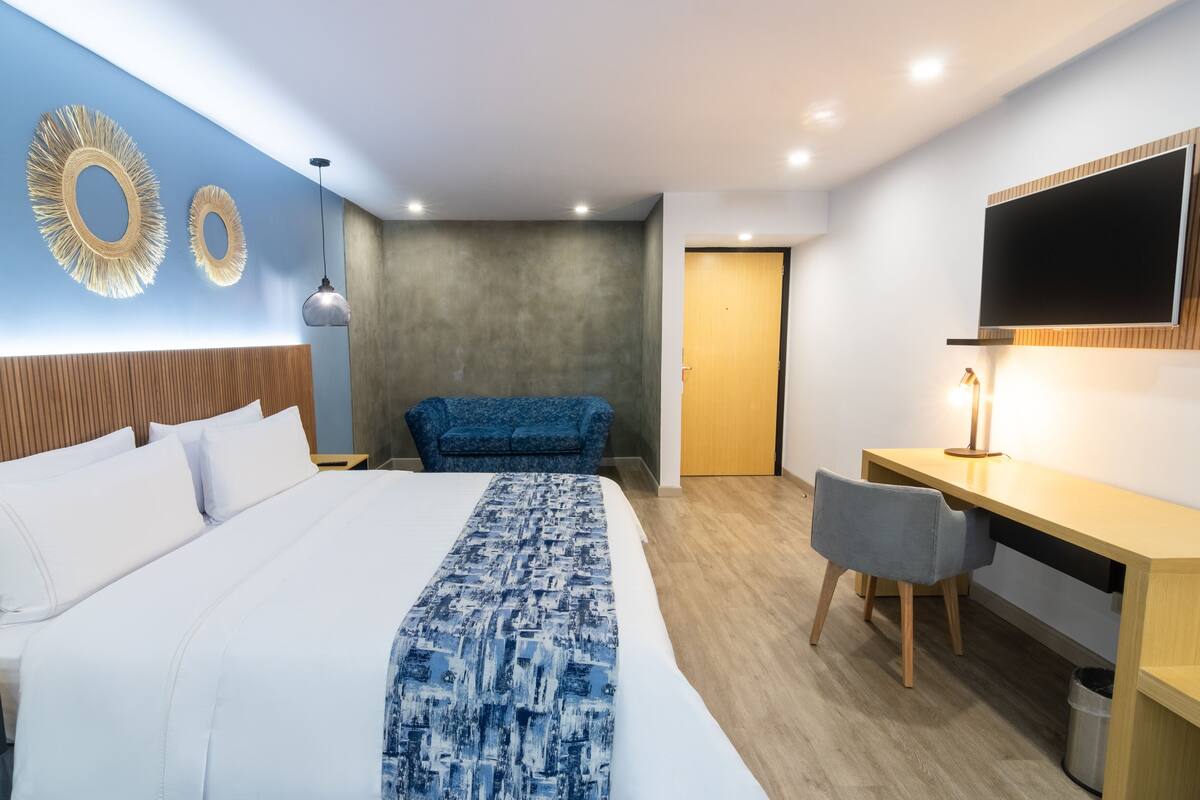 A modern hotel room with a large bed, a desk, a chair, a television, and decorative wall mirrors.