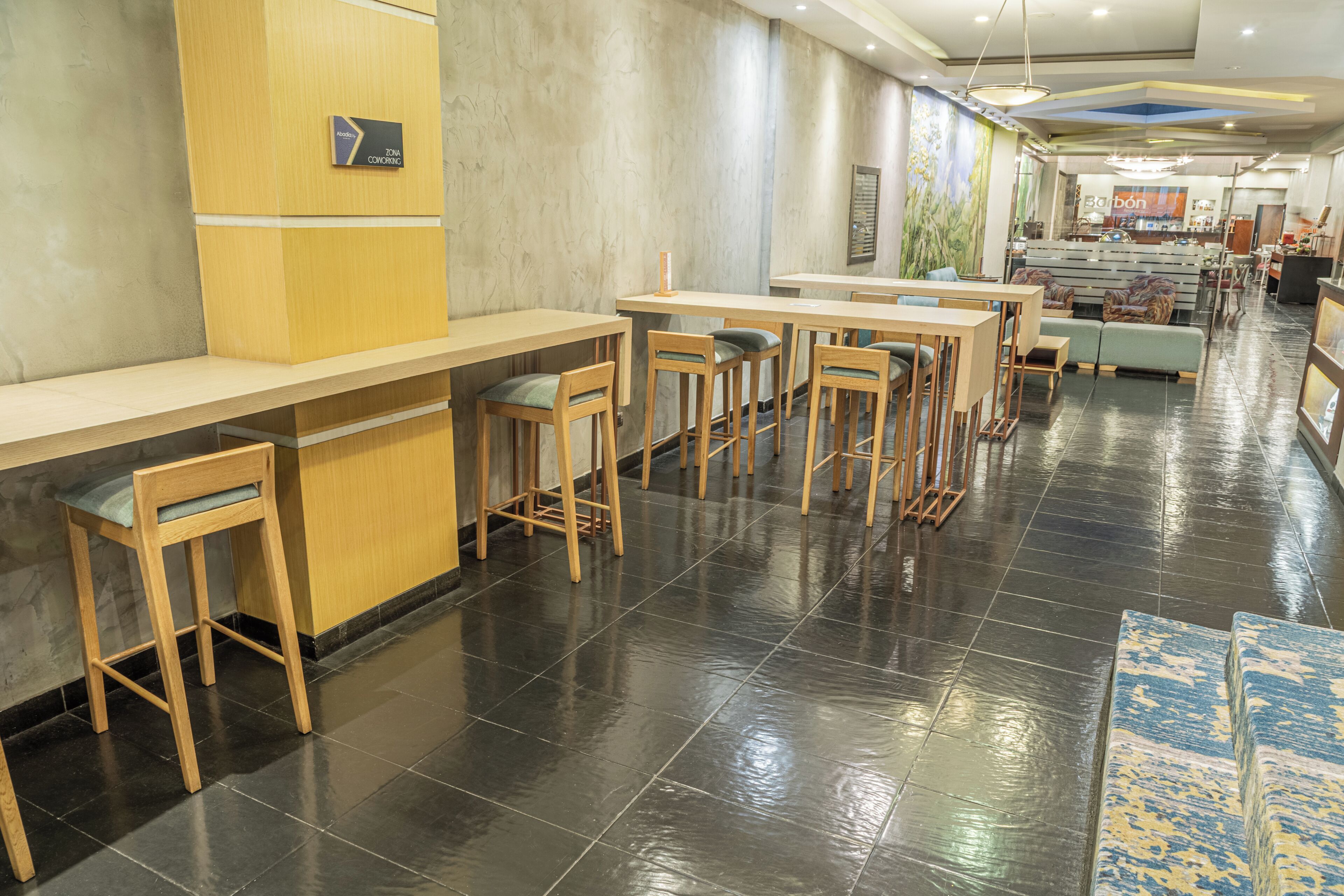 A modern hotel lobby with a long reception desk, multiple bar stools, and a seating area with sofas and chairs.