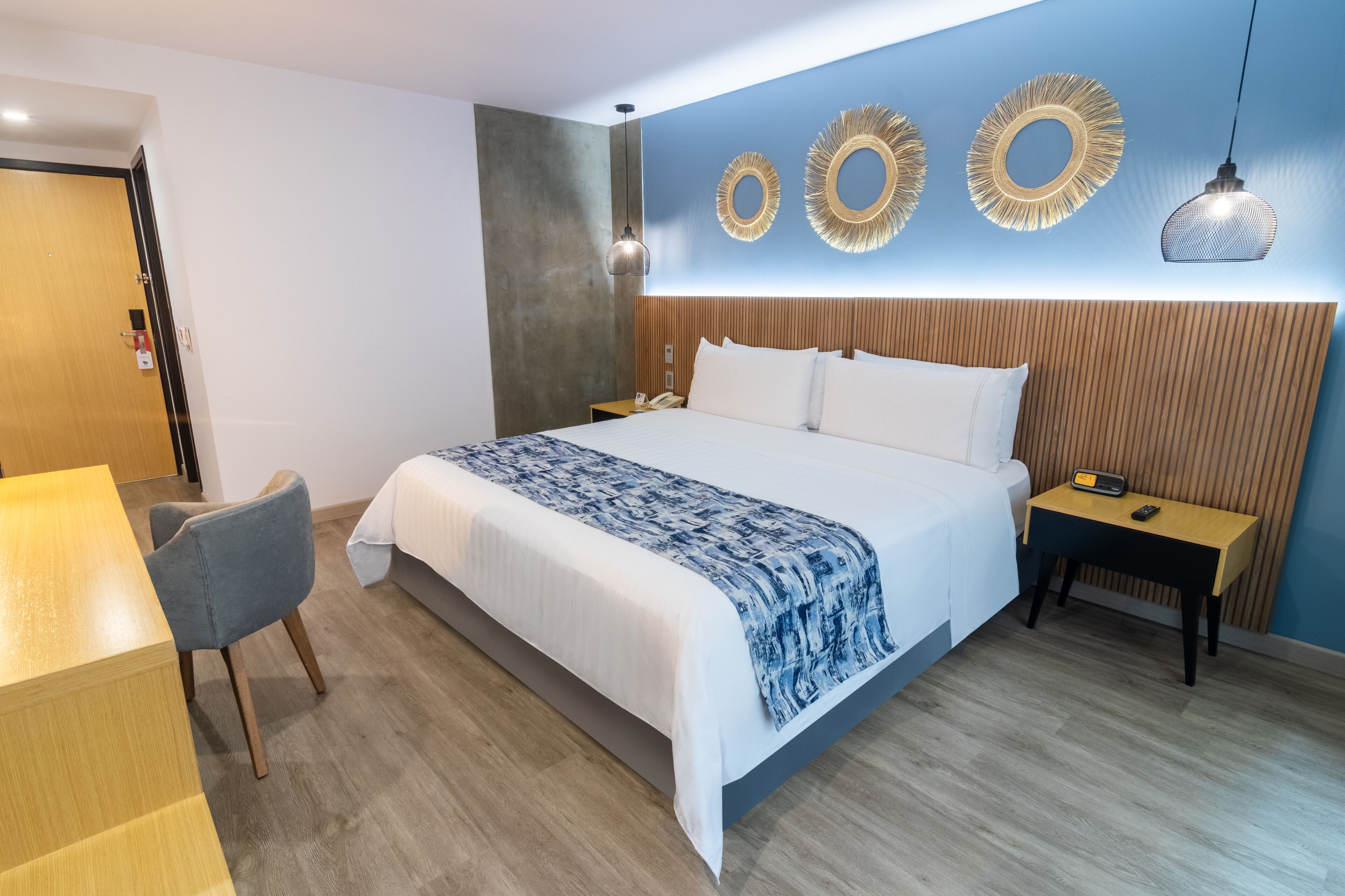 Une chambre d’hôtel moderne avec un grand lit, une table de chevet avec une lampe, une chaise et un bureau.
