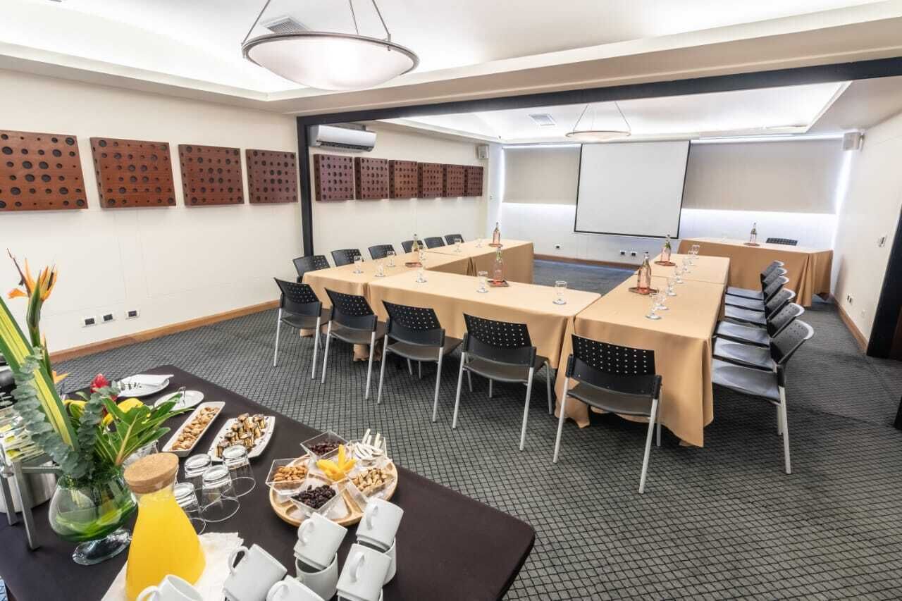 A conference room with a long table, chairs, a projector screen, and a buffet table with food and drinks.