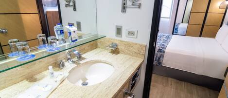 Un baño moderno con lavamanos de mármol, un espejo grande y una cama con colcha de rayas azules y blancas.
