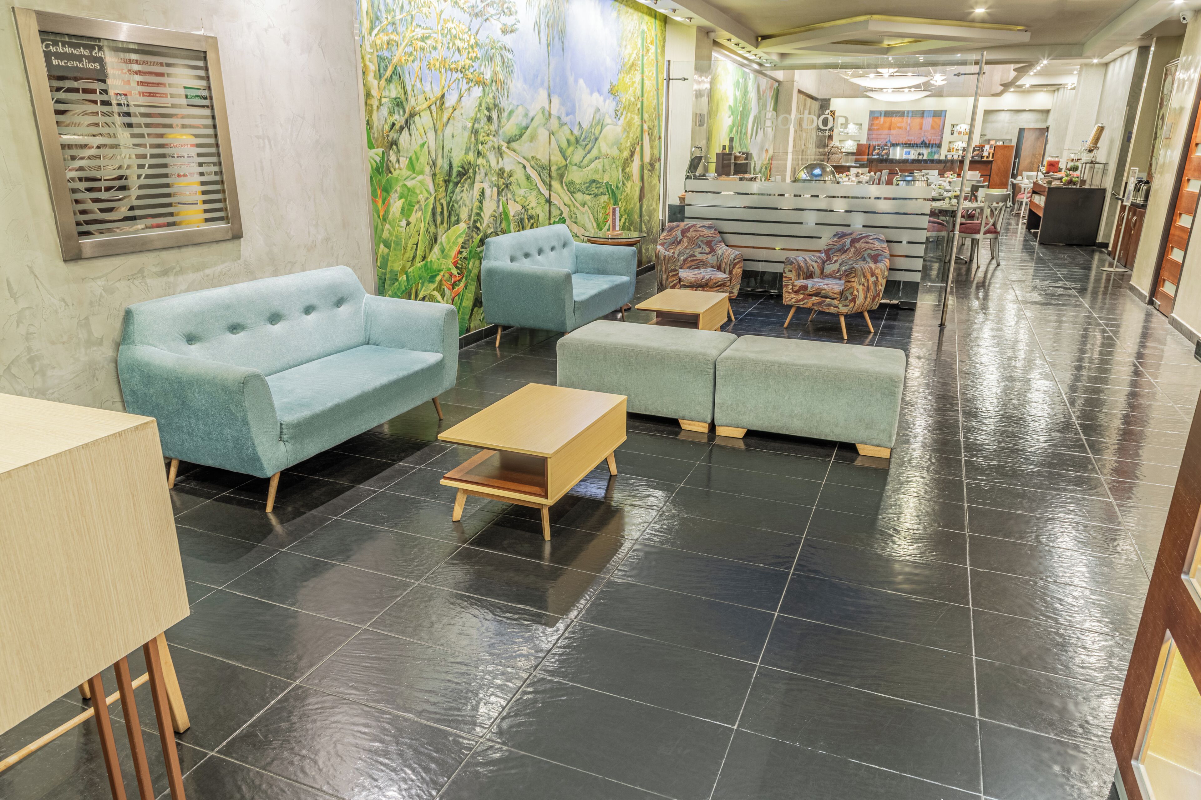 A hotel lobby with seating areas, a reception desk, and a mural on the wall.