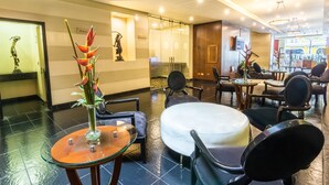 Een hotel lobby met een receptiebalie, een zithoek en uitzicht op de straat.
