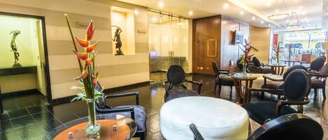 Een hotel lobby met een receptiebalie, een zithoek en uitzicht op de straat.