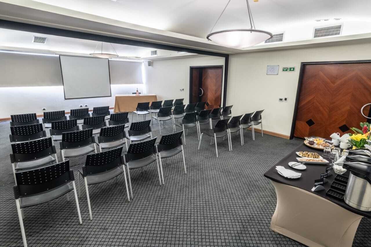 Une salle de conférence avec des rangées de chaises, un écran de projection, un pupitre et une table de buffet garnie de nourriture et de boissons.