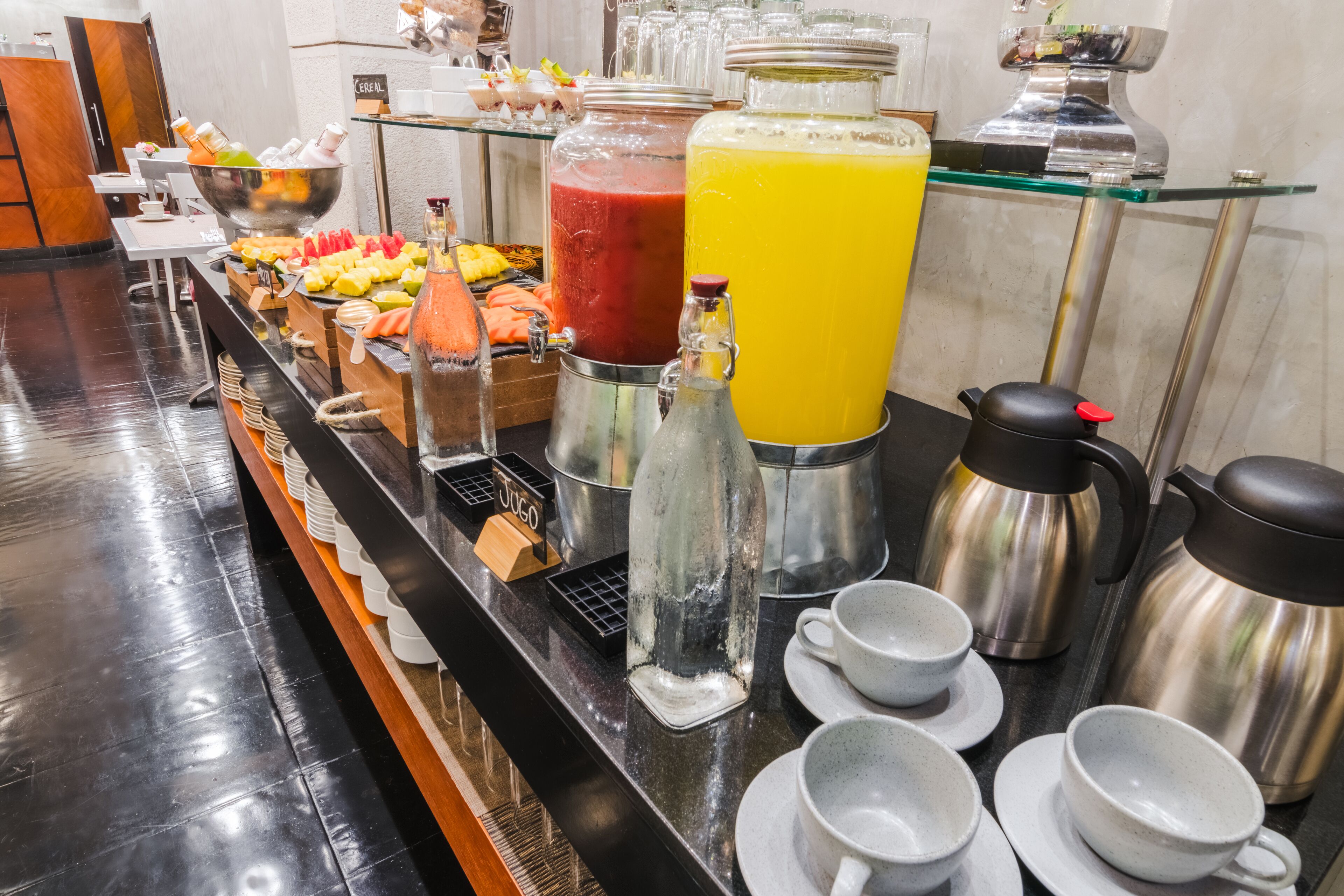 Un bufé con diferentes opciones de comida y bebidas, incluyendo un refresco amarillo grande, un refresco rojo y una variedad de frutas.