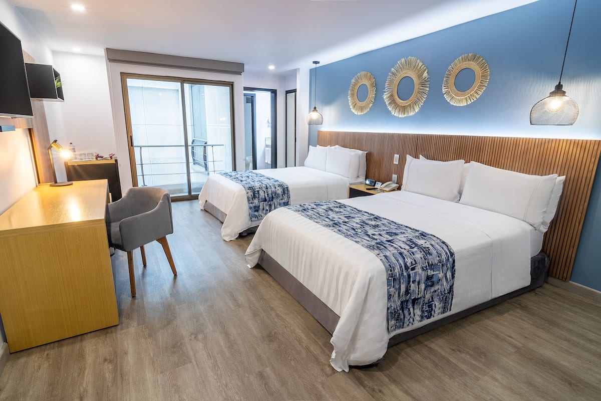 A hotel room with two beds, a desk, a chair, and a balcony.