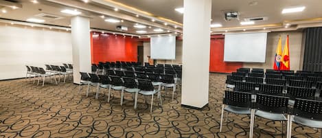 A conference room with rows of chairs, a projector screen, and flags.