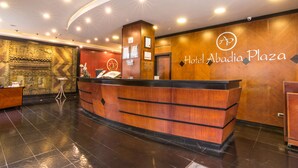 Een hotel receptie met een houten balie, een wandbord en een patroonbehang in de achtergrond.