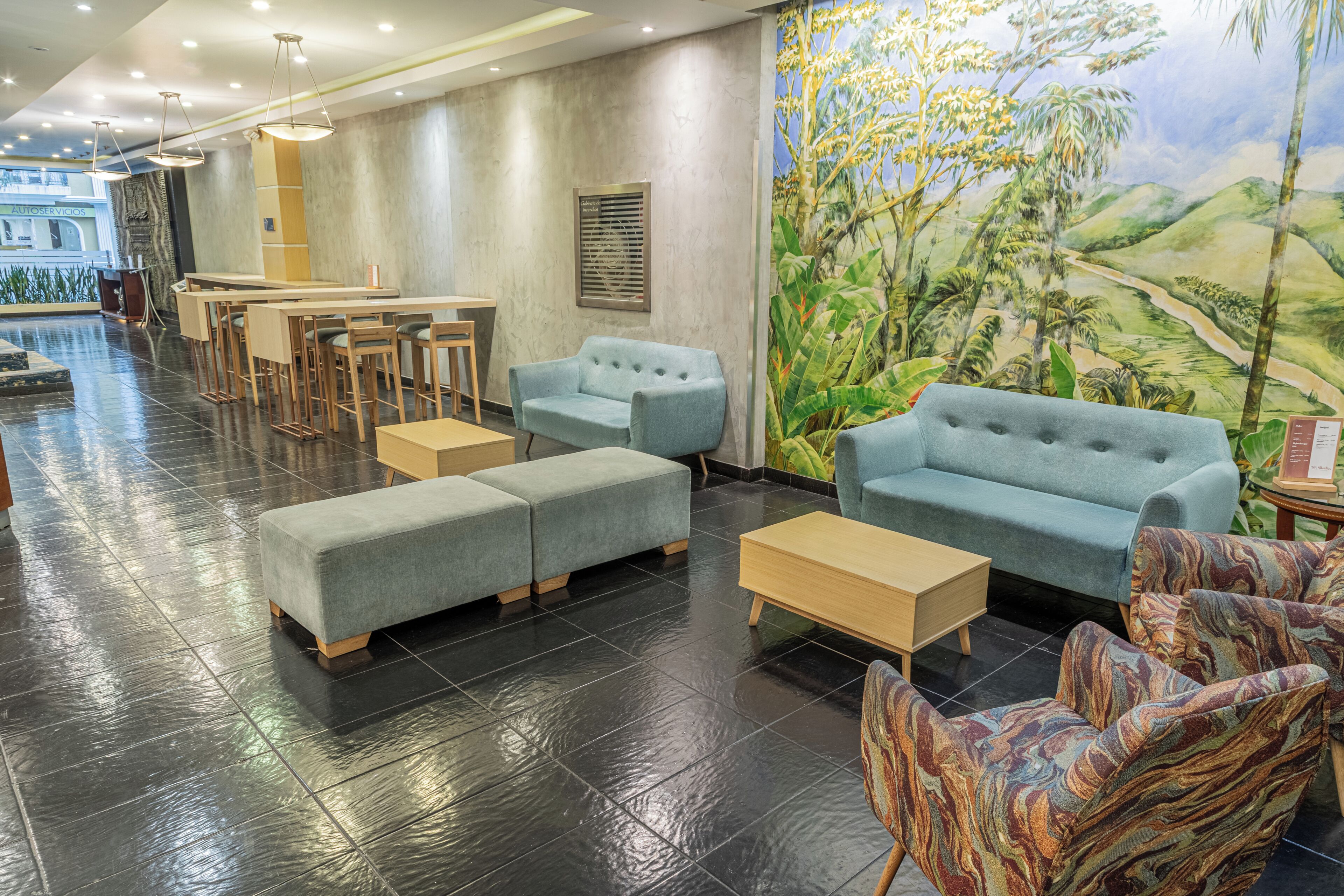 A hotel lobby with seating arrangements, a reception desk, and a mural of a tropical landscape.