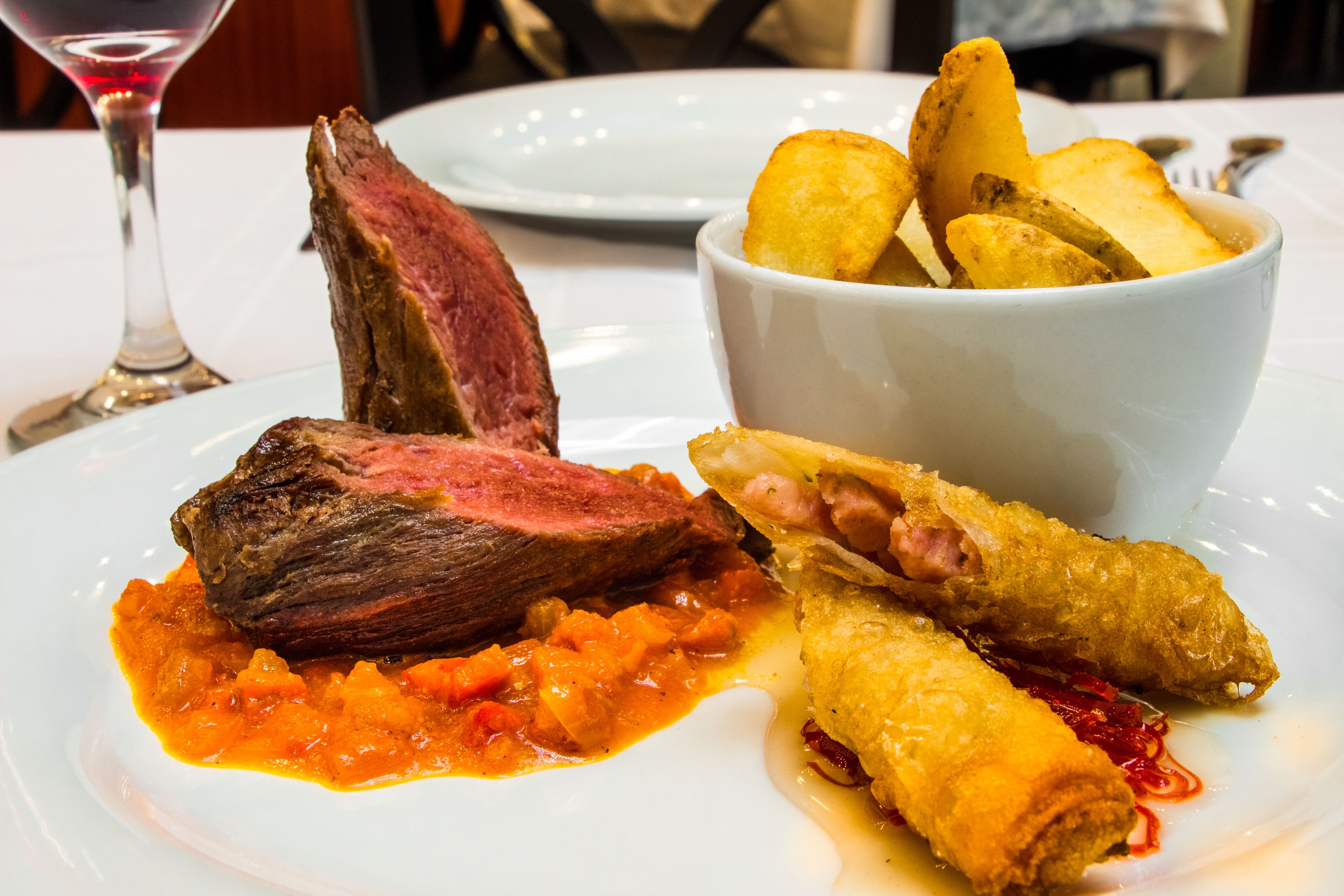 A plate with steak, fries, and spring rolls.