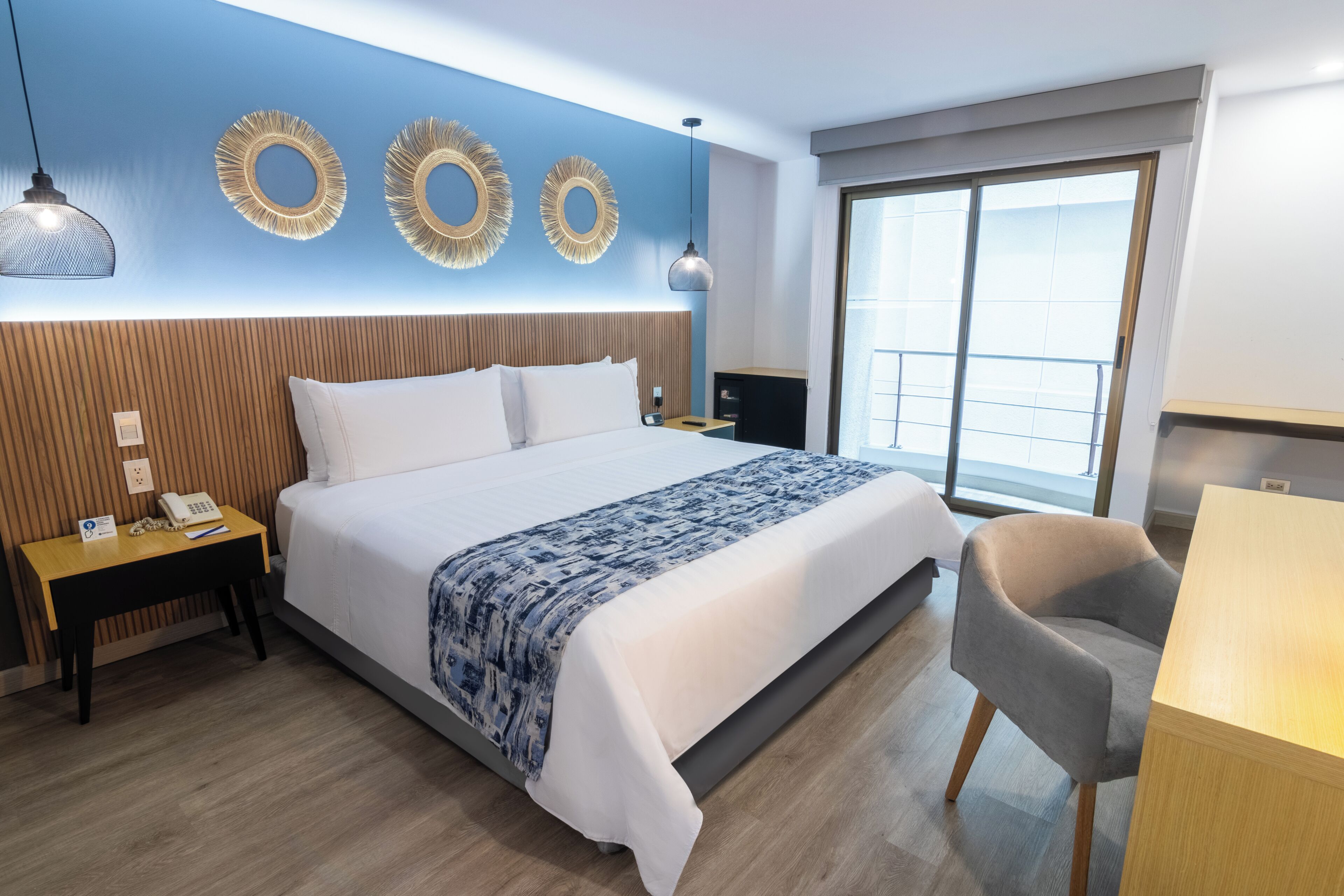 A hotel room with a bed, bedside table, chair, and a large window.