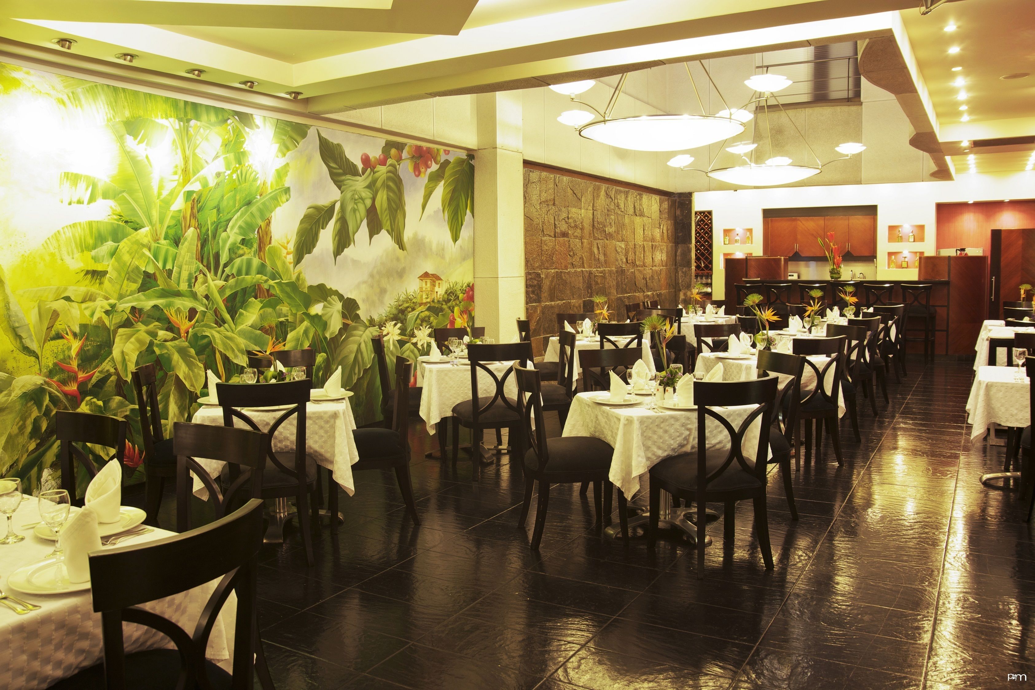 A restaurant with multiple tables and chairs, a large mural with plants, and a kitchen area in the background.
