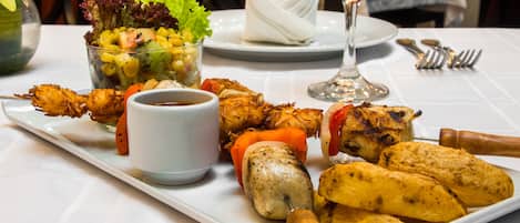 A dining table with a variety of skewered meats, a bowl of salad, and a glass of red wine.