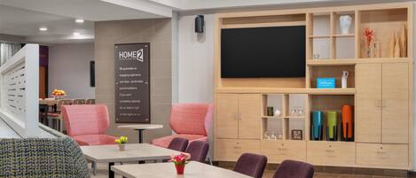 A hotel lobby with seating, a TV screen, and a sign about a home guarantee.
