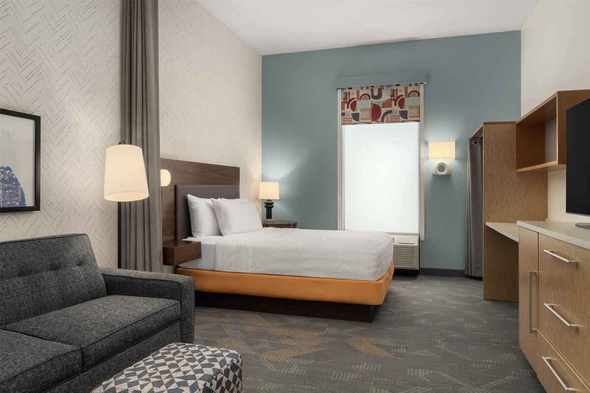 A hotel room with a bed, a sofa, a TV, and a desk.