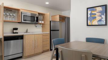 A compact kitchen with modern appliances, wooden cabinets, and a dining area with blue chairs.