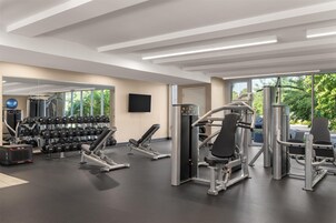 Un gimnasio moderno con diversos equipos de ejercicio, ventanas amplias y un espejo en la pared.