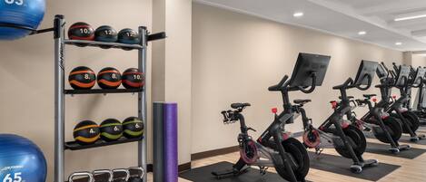 Un gimnasio con bicicletas estáticas, un soporte para balones medicinales y mancuernas.