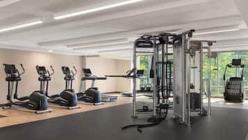 Un gimnasio con cintas de correr, máquinas de pesas y vistas a zonas verdes a través de amplias ventanas.