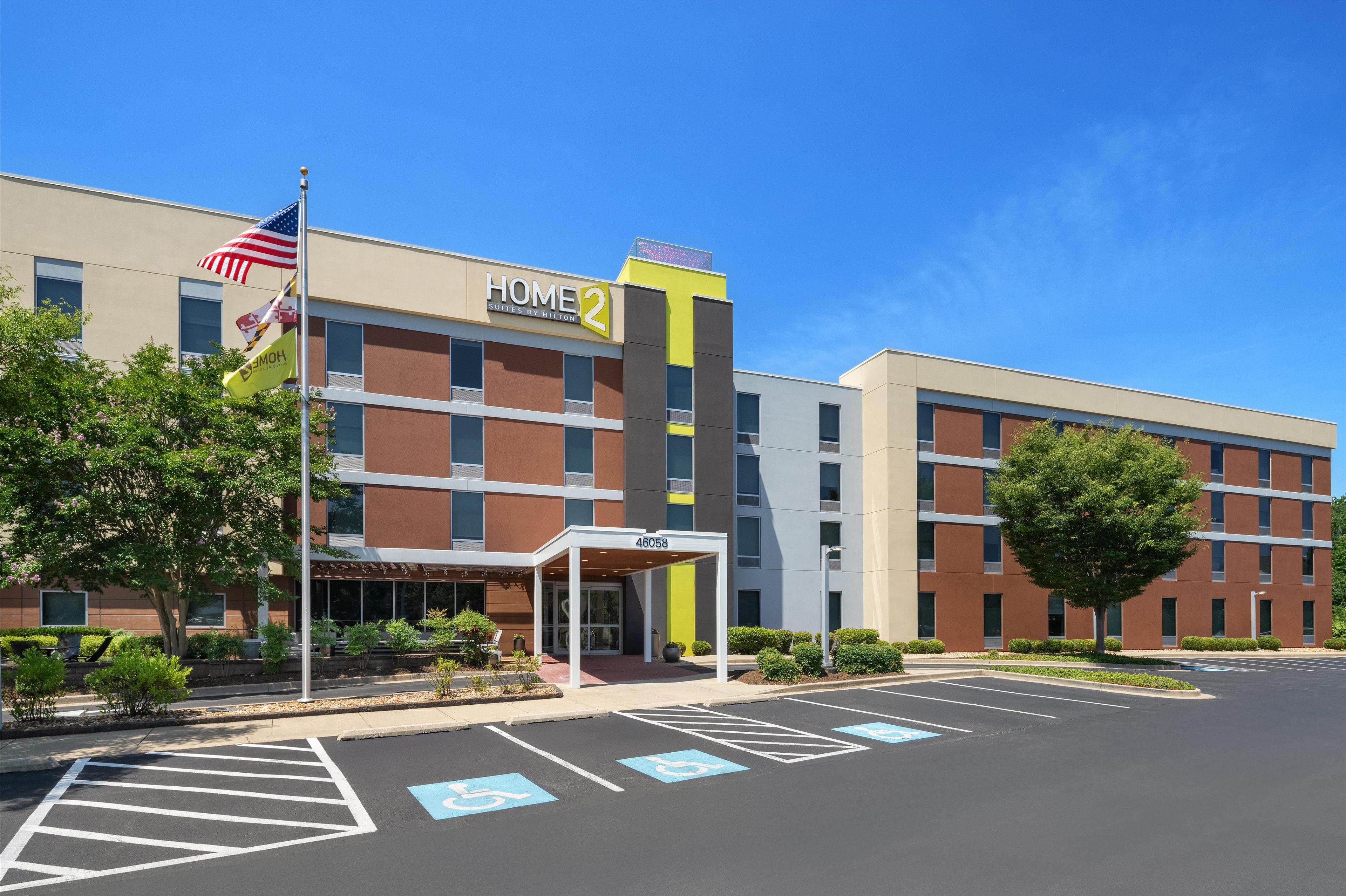 A modern hotel with a "Home 2" sign, a covered entrance, and a parking lot with handicapped parking spaces.
