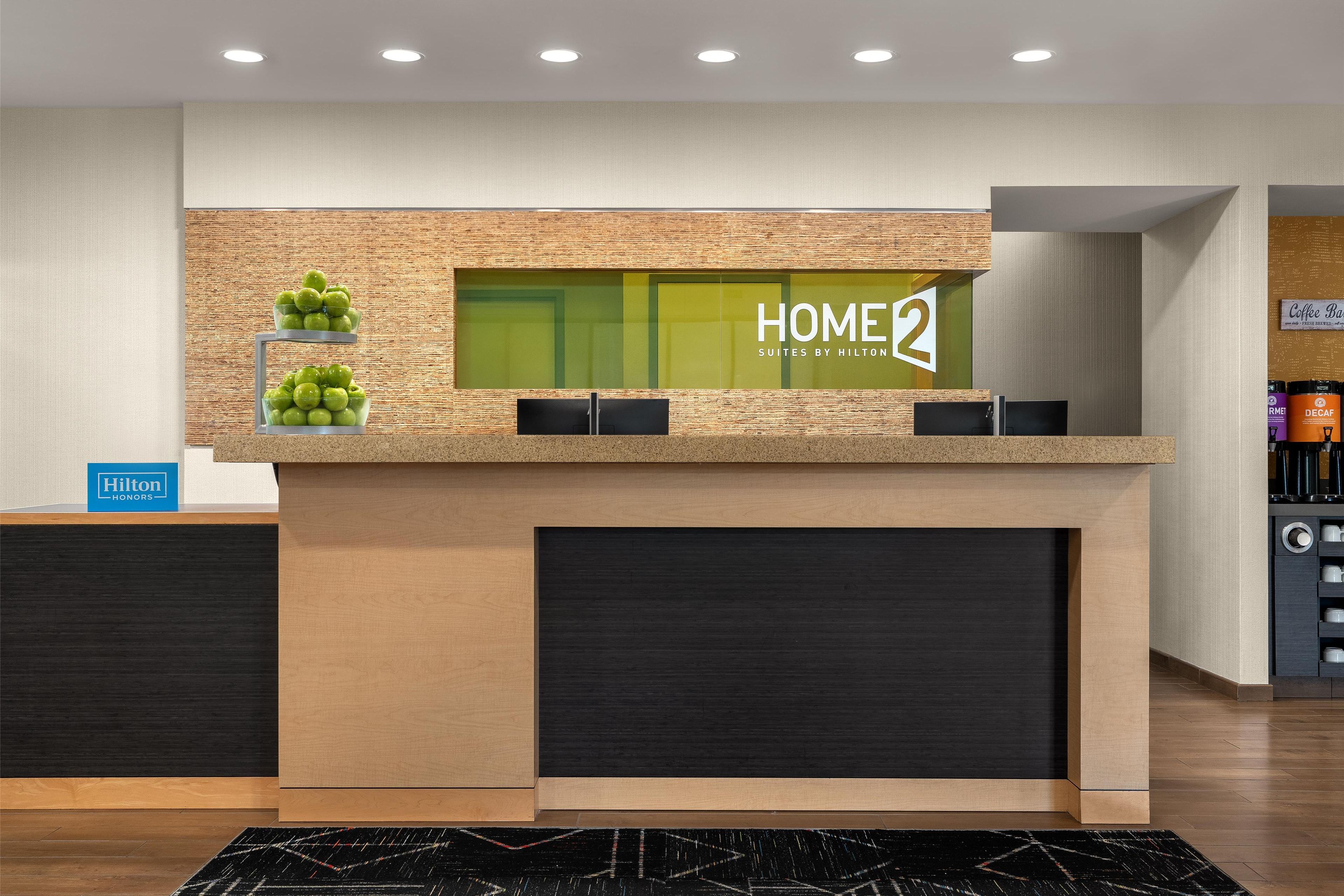 A reception desk with a 'HOME2' sign, a 'Hilton Honors' sign, and a coffee bar in the background.