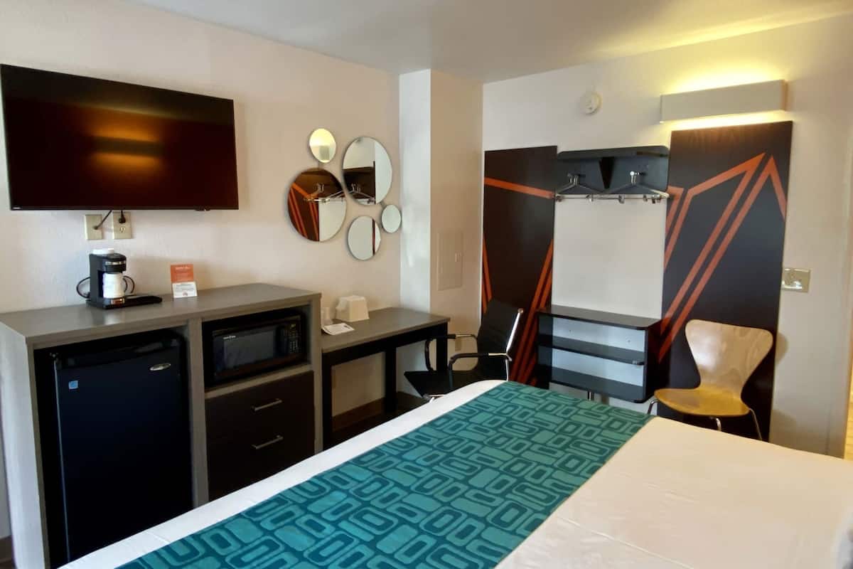 Hotellihuone, jossa on sänky, työpöytä, kahvinkeitin, televisio, peili ja tuoli.