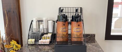 Una estación de café con dos máquinas de espresso, un dispensador de café y una bandeja de vasos desechables.