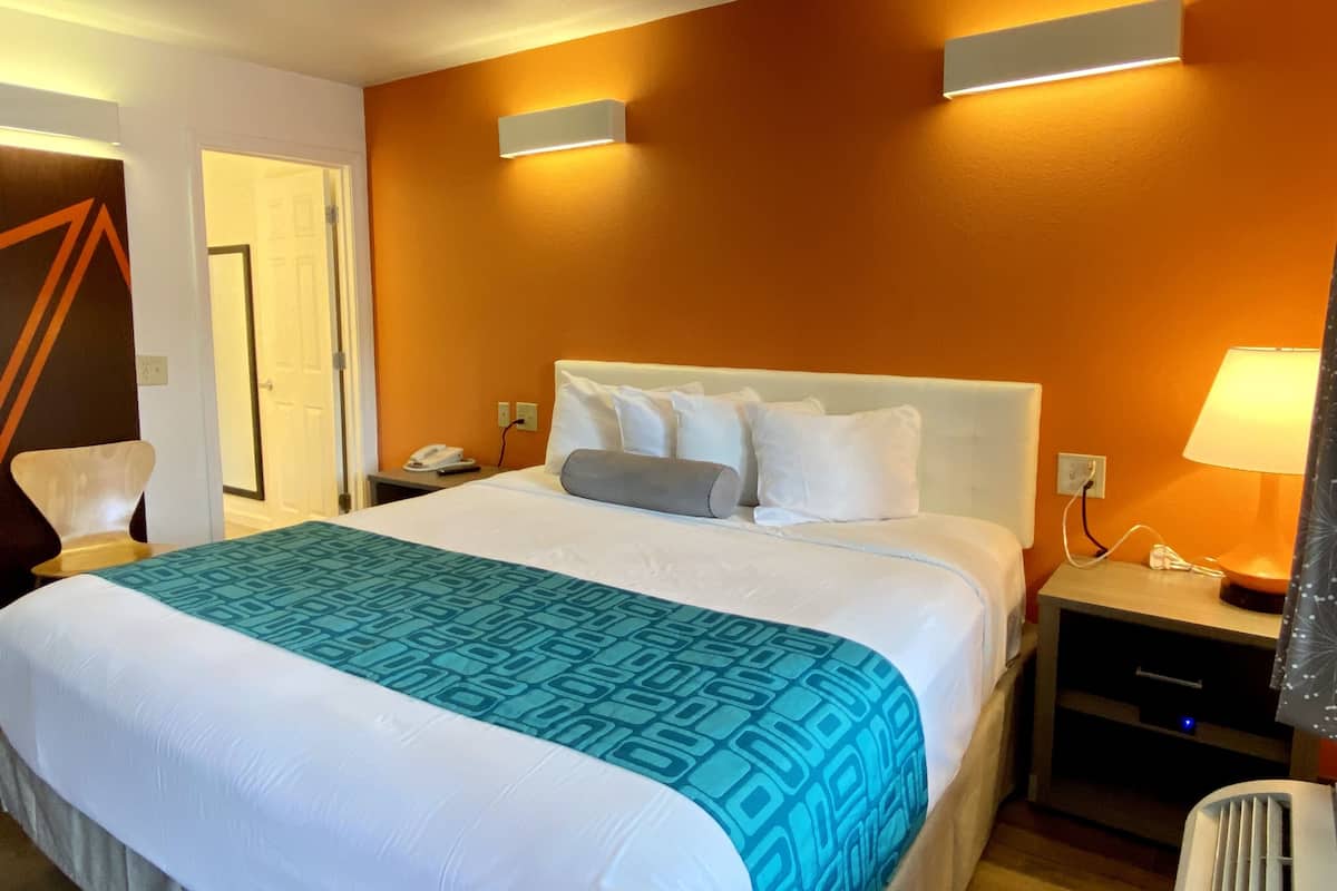 Hotellihuone, jossa on suuri sänky, yöpöytä, lamppu ja seinään kiinnitetty valaisin.