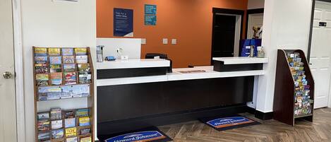 A reception area with a wooden reception desk, a bulletin board with travel brochures, and a wooden floor.