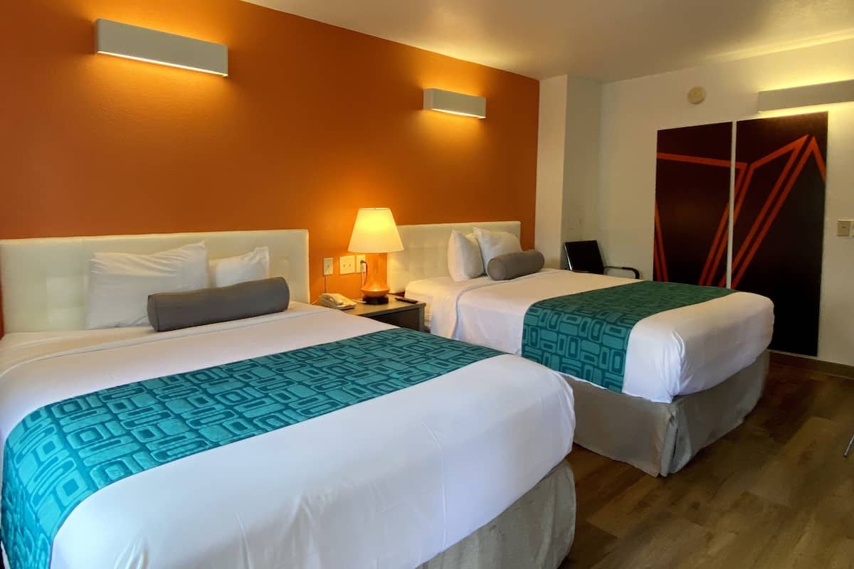 Hotellihuone, jossa on kaksi sänkyä, yöpöytä lampun kanssa, puhelin ja tuoli.