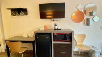 A compact hotel room with a kitchenette, a flat-screen TV, a coffee maker, a microwave, and a seating area with two chairs.