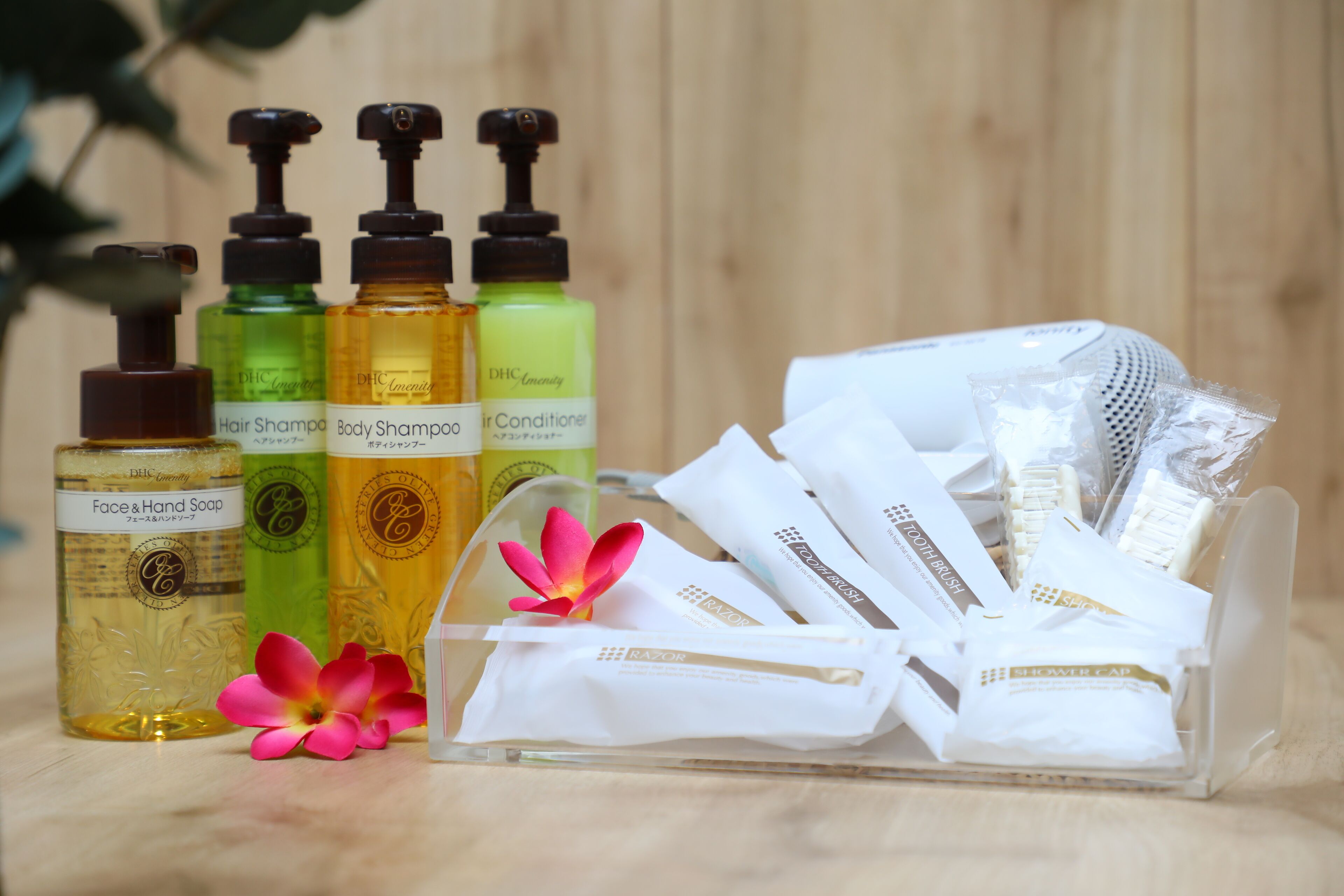 Une collection de produits de toilette comprenant un shampooing pour les cheveux et le corps, un après-shampooing, ainsi qu’un savon pour le visage et les mains, accompagnée d’accessoires de soin tels que des rasoirs et une brosse, le tout disposé sur une surface en bois.