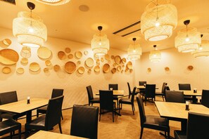 A restaurant with multiple tables and chairs, and a wall decorated with circular woven items.