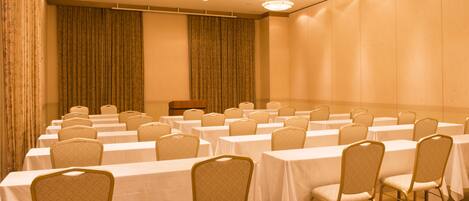 A conference room with rows of tables and chairs, a podium, and curtains.