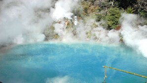 Un manantial de aguas termales con agua azul cristalina, rodeado de rocas y vegetación.