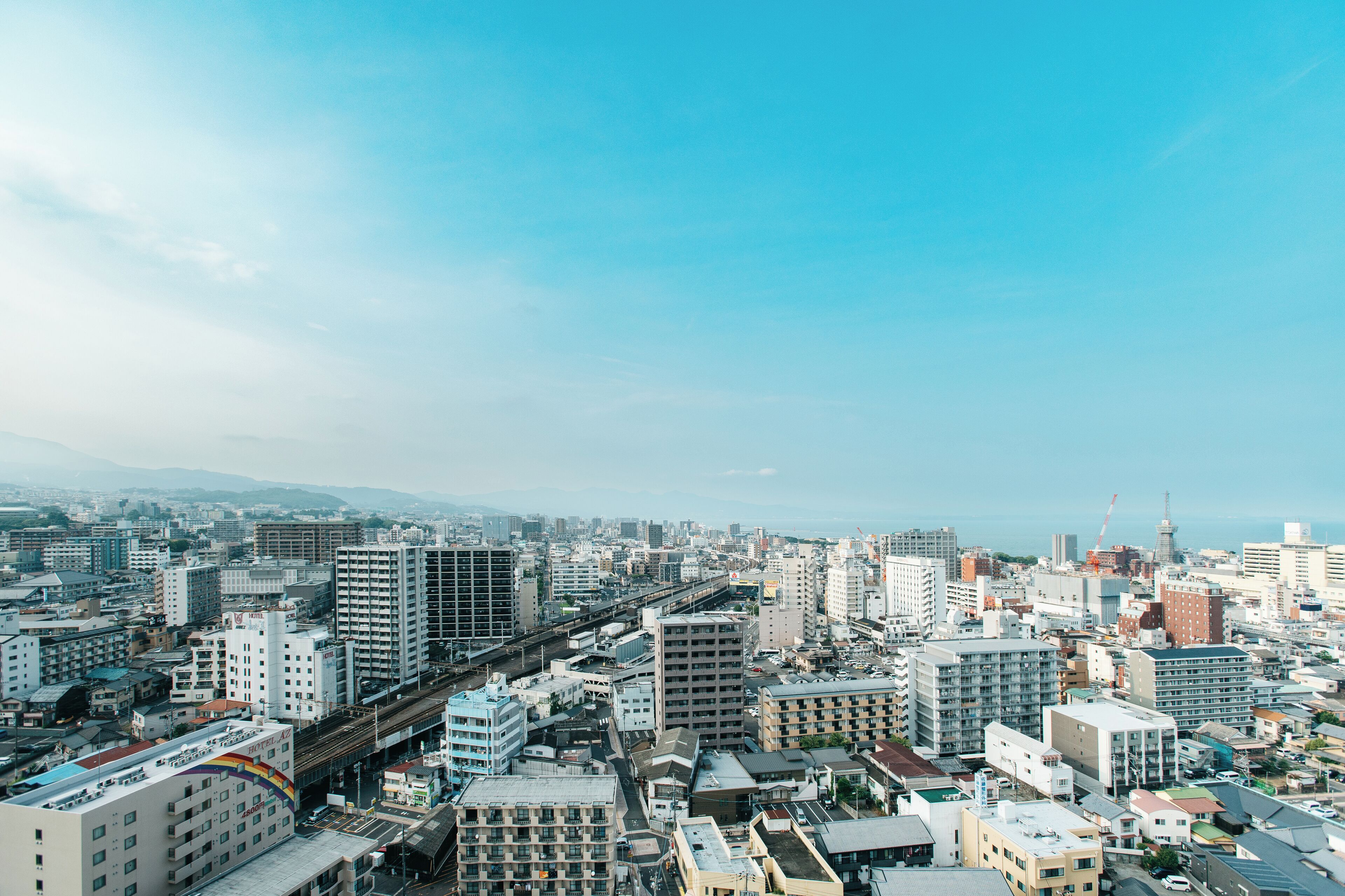 A cityscape with high-rise buildings, a prominent train track, and a distant view of mountains.