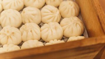 A close-up of a wooden tray filled with round, white steamed buns with a decorative pattern on top.