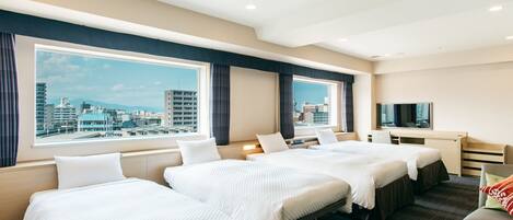 A hotel room with two beds, a desk, a TV, and a view of the cityscape.