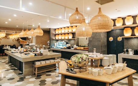 A modern cafe with a central island, wicker pendant lighting, and a variety of bowls and plates on display.