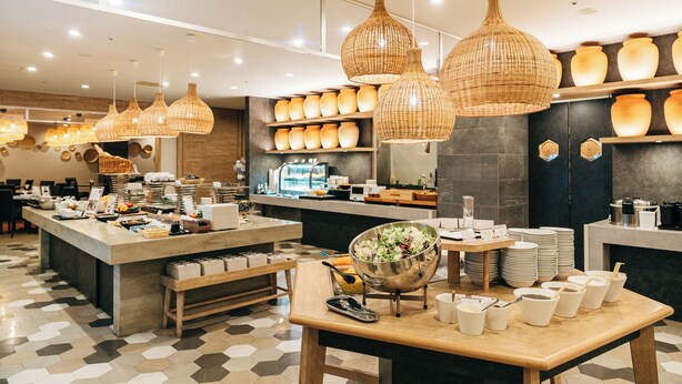 Un café moderno con una isla central, luminarias colgantes de mimbre y una variedad de cuencos y platos a la vista.
