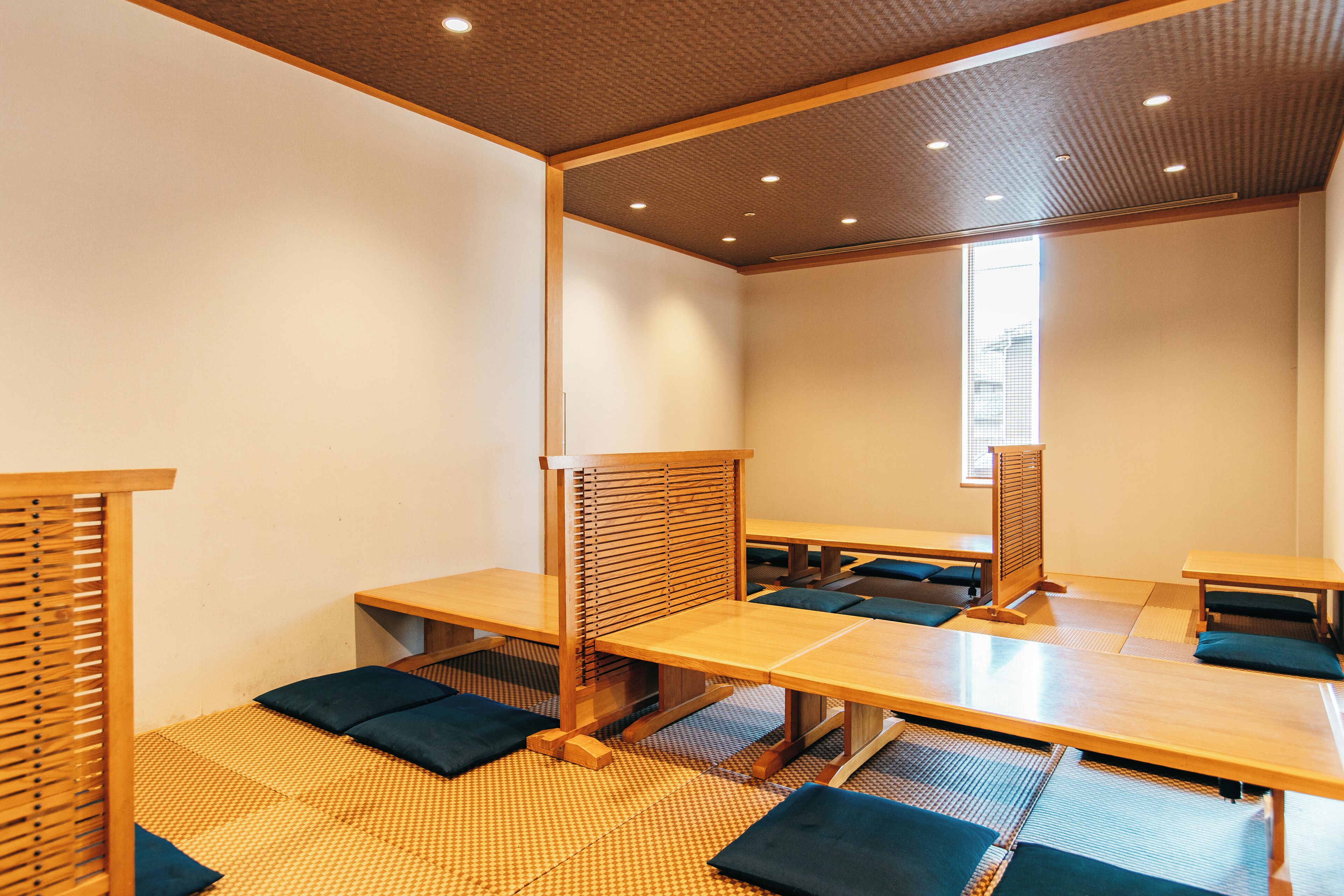 A room with tatami mats, low wooden tables, and cushions.