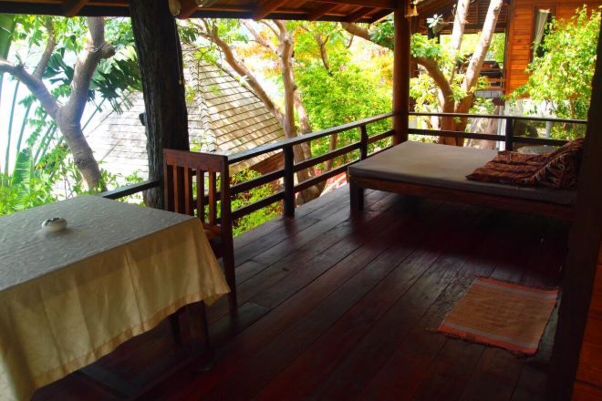 A wooden deck with a table and bench, surrounded by lush greenery and trees.