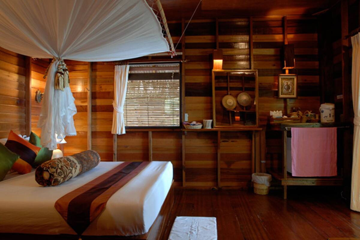 A wooden cabin room with a bed, a small table, and a shelf with decorative items.