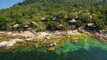 Un resort tropical con bungalows de techo de paja rodeado de exuberante vegetación y aguas cristalinas.