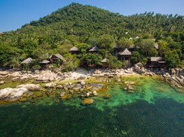 Un resort tropical con bungalows de techo de paja rodeado de exuberante vegetación y aguas cristalinas.
