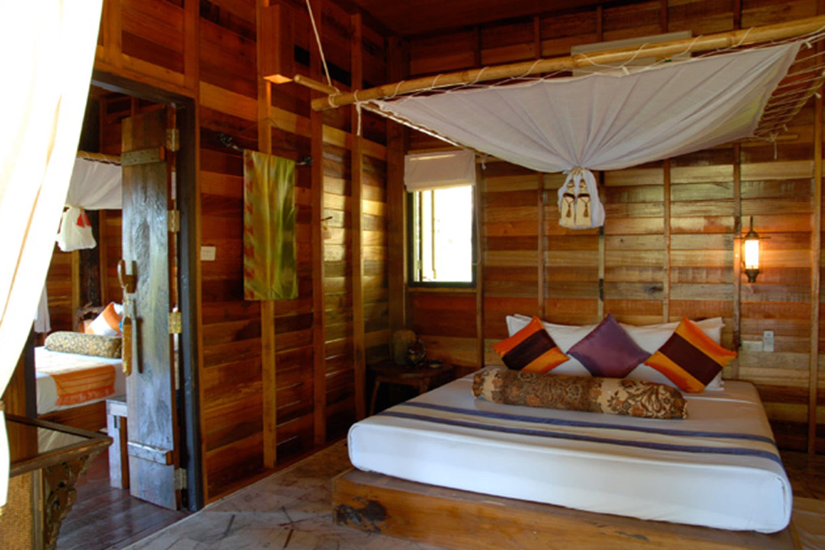Een houten kamer met een bed, nachtkastje, raam en klamboe.