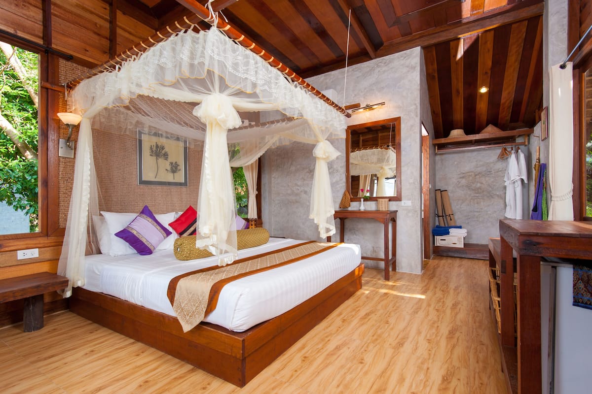A wooden four-poster bed with a canopy, a bedside table, a bench, and a mirror.