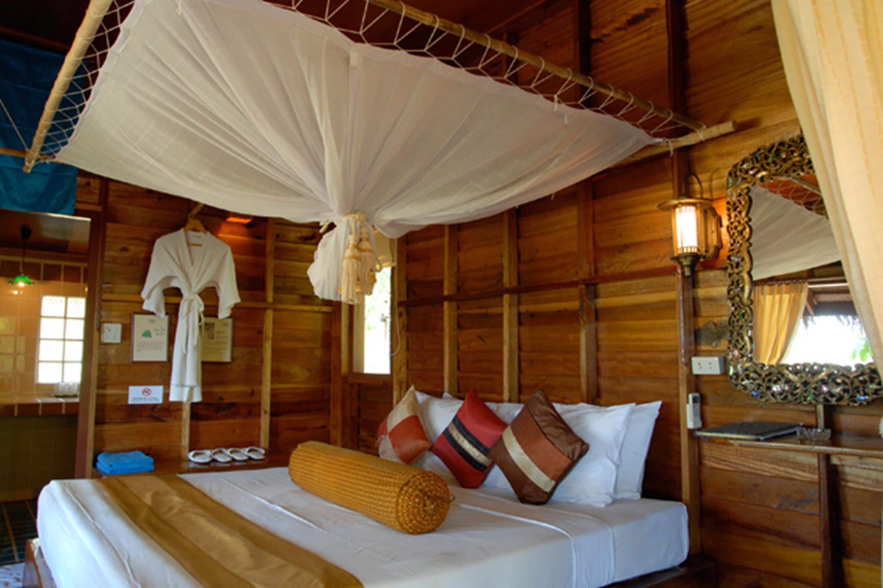 A wooden cabin bedroom with a bed, pillows, a hanging white robe, and a mirror.