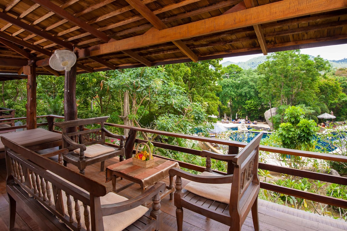 A wooden deck with seating and a pool, surrounded by lush greenery and mountains.